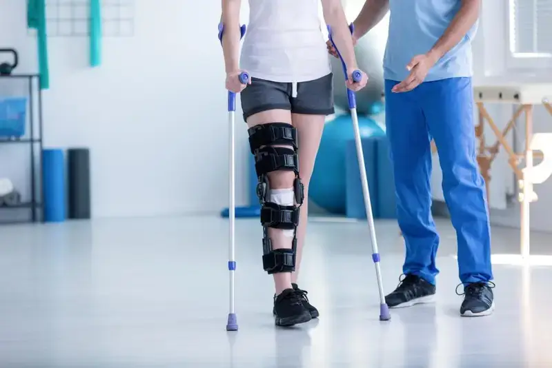 مريض يستخدم جهاز مشي بمساعدة أخصائي علاج طبيعي بعد إجراء عملية في الساق.